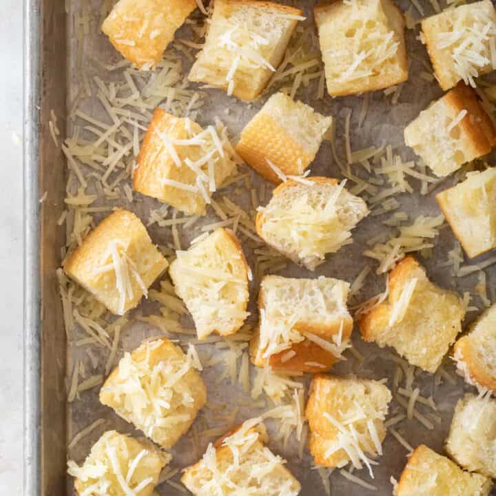 A cookie sheet filled with bread cubes tossed in butter and Parmesan cheese for Parmesan croutons.