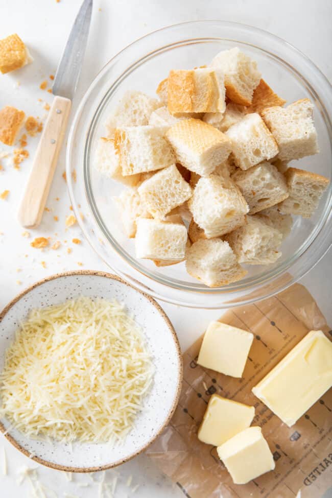 A glass bowl filled with pieces of cubed bread next to slices of butter.