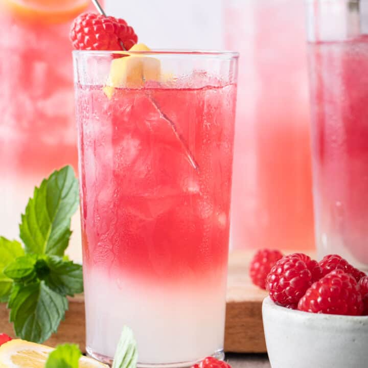 Four glasses filled with pink lemonade. A small bowl of raspberries sits next to the glasses.