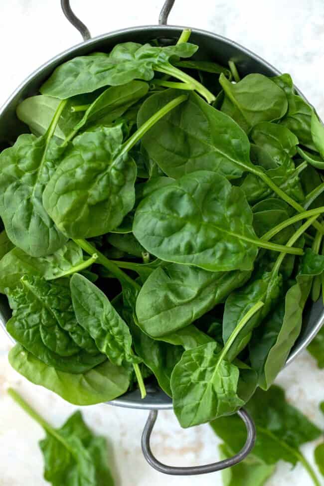 A metal colander filled with fresh green spinach leaves.