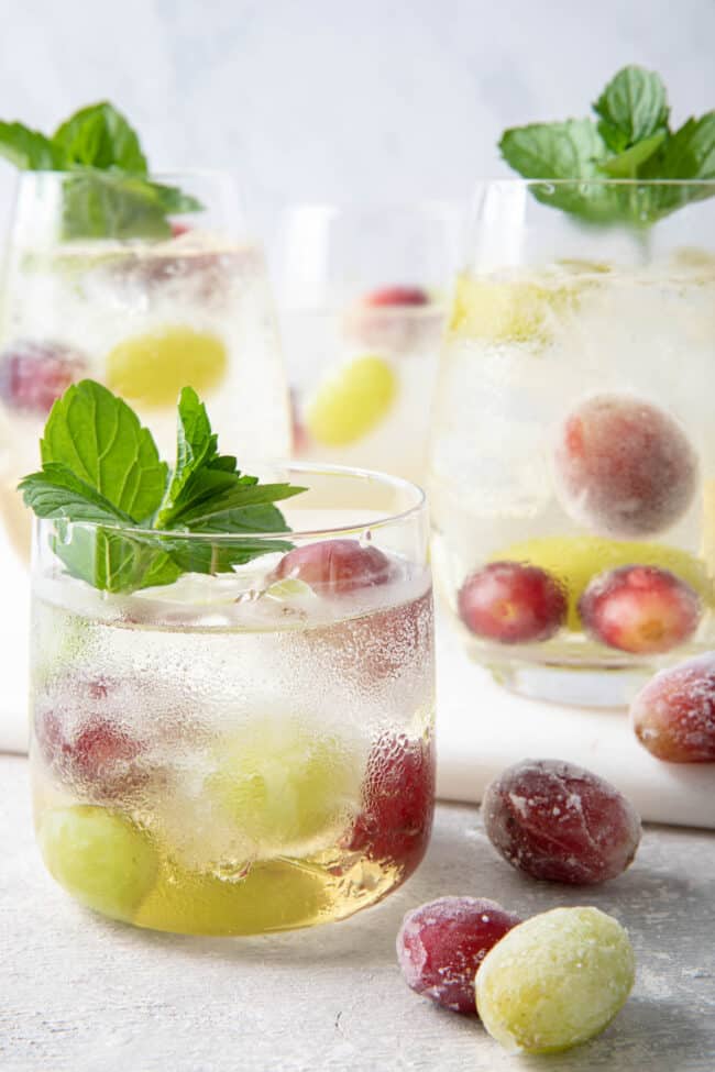 4 clear glasses filled with white grape juice and sparkling water and frozen grapes. Sprigs of mint garnish the glasses.