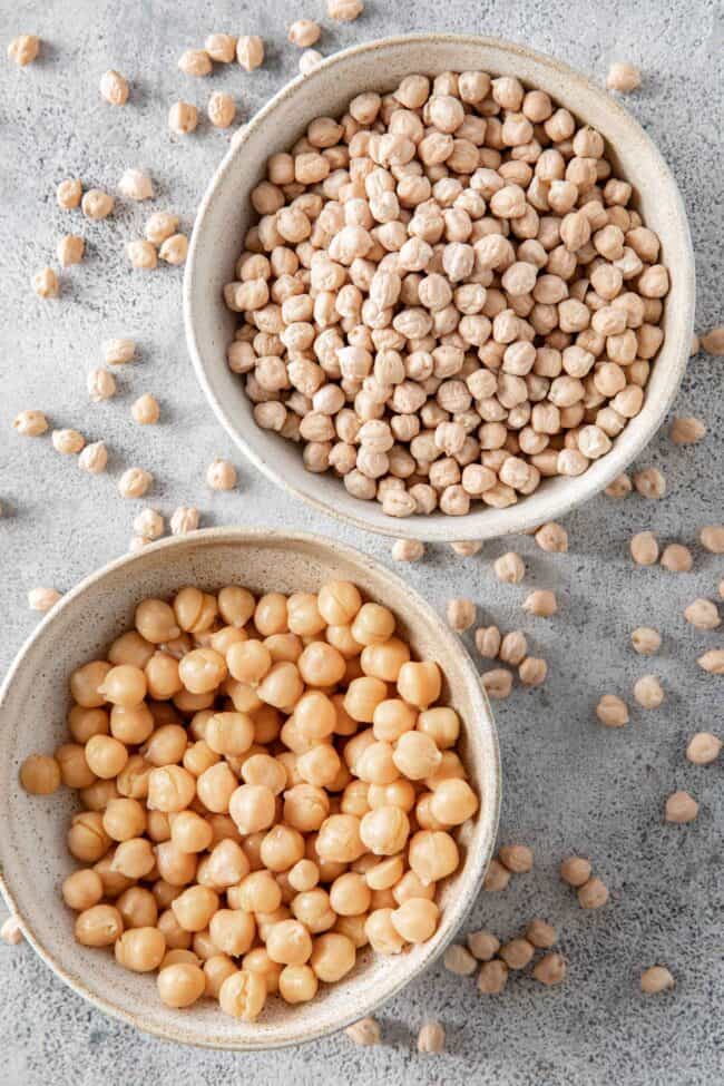 Two bowls filled with chickpeas - one cooked and one raw. Dry chickpeas are scattered on the board around the bowls - for are chickpeas gluten free