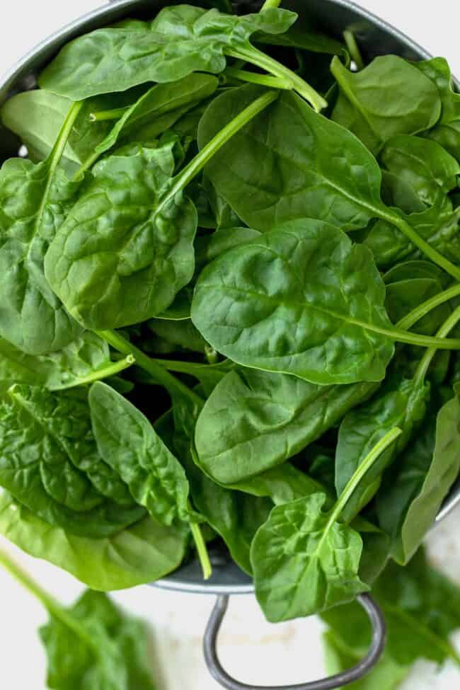 A silver colander filled with green spinach leaves.