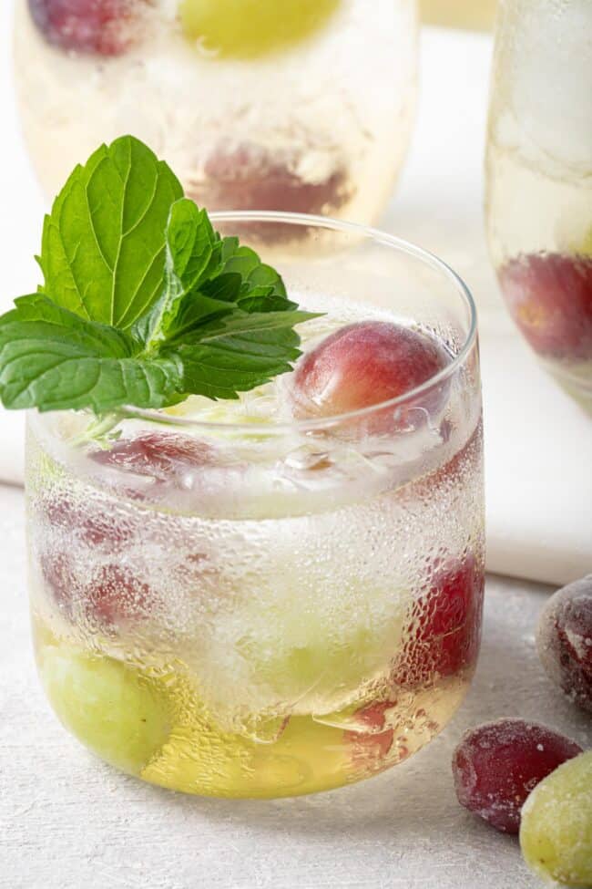 a clear glass filled with white grape non alcoholic spritzer and frozen grapes. A sprig of mint garnishes the glass.