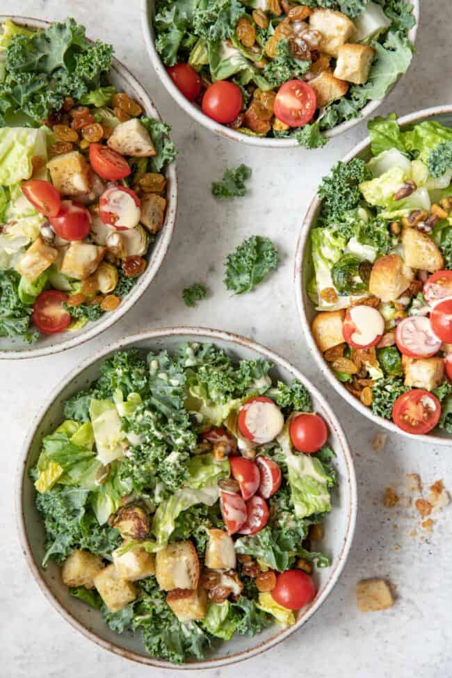 Four bowls filled with Kale Caesar Salad (kale, Romaine lettuce, cherry tomatoes and croutons)