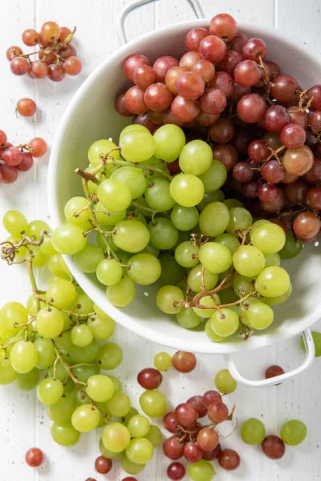 A white colander filled with red and green grapes