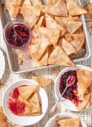 A cookie sheet filled with fried cinnamon tortilla chips. Two white plates with the chips on them sits next to the cookie sheet.