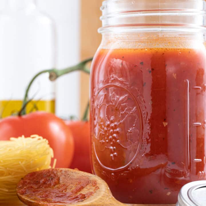A clear glass mason jar filled with marinara sauce. A wooden spoon sits next to the jar.