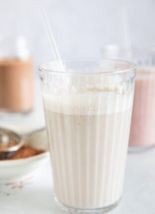 Three clear glasses filled with vegan milk. One banana almond milk, one chocolate banana milk and one strawberry banana milk.