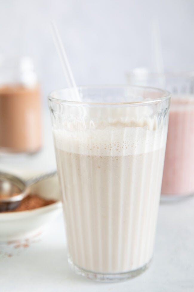 Three clear glasses filled with vegan milk. One banana almond milk, one chocolate banana milk and one strawberry banana milk.