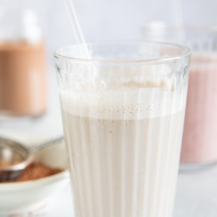 Three clear glasses filled with vegan milk. One banana almond milk, one chocolate banana milk and one strawberry banana milk.