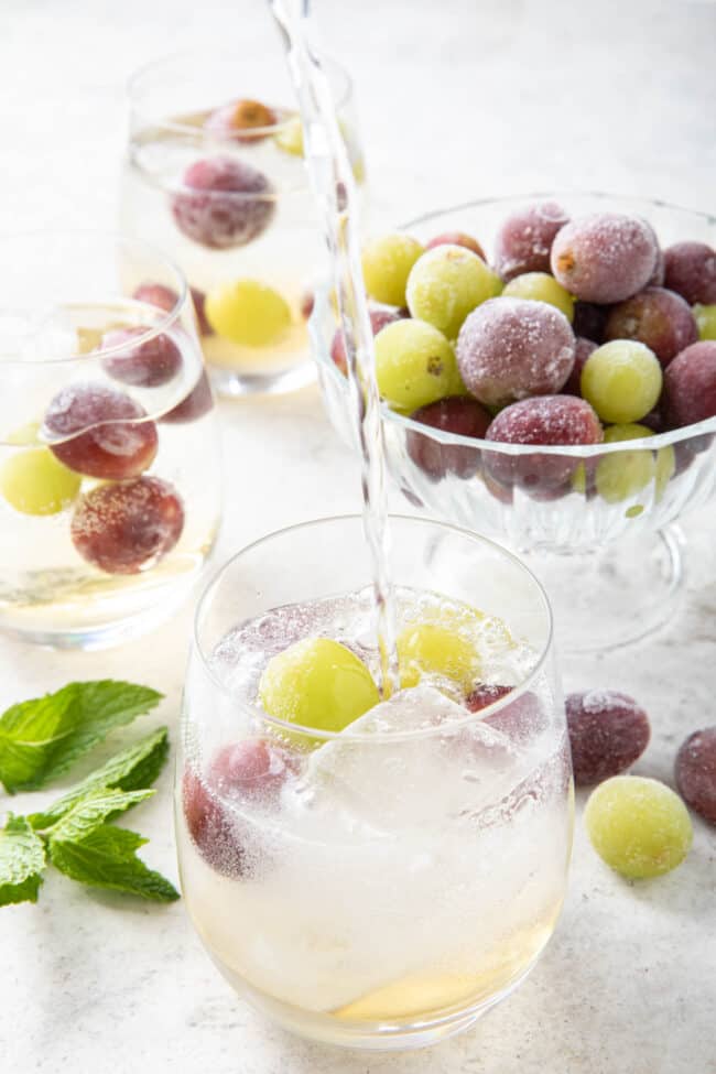 Three clear glasses with frozen grapes and ice and clear liquid in them.