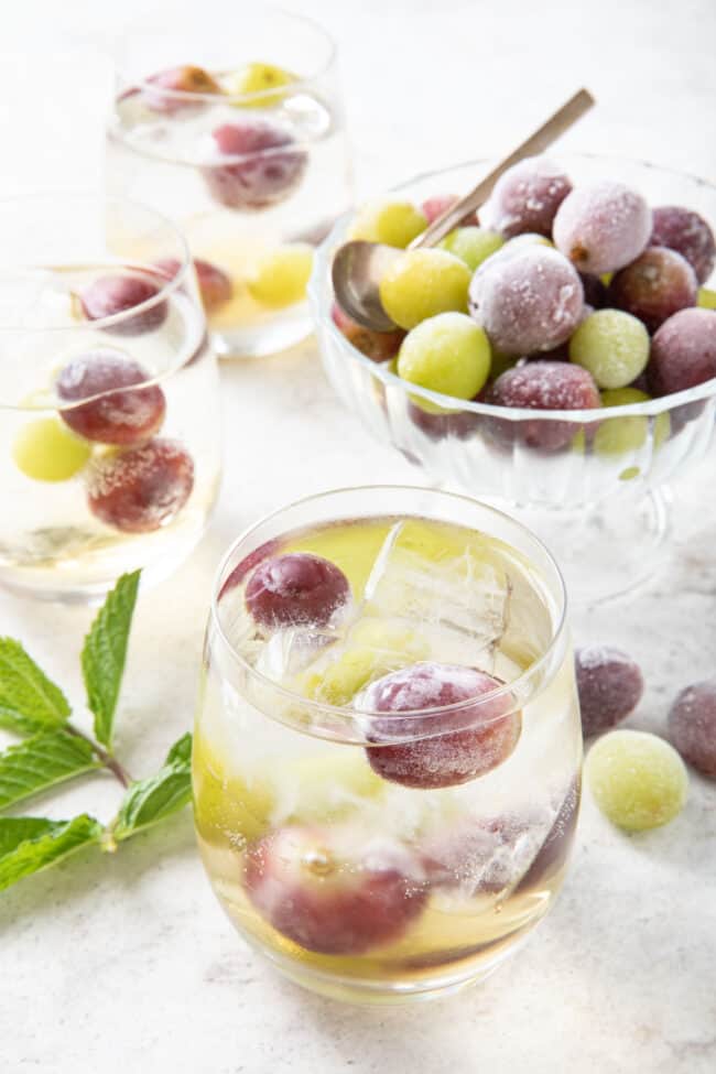 Three clear glasses with frozen grapes and ice and clear liquid in them.