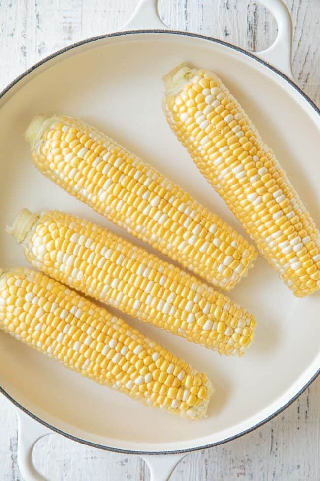 Four corn on the cob in a white pot filled with water.