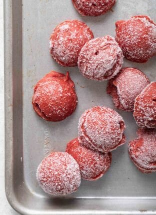 Several balls of frozen tomato paste are scattered on a cookie sheet.