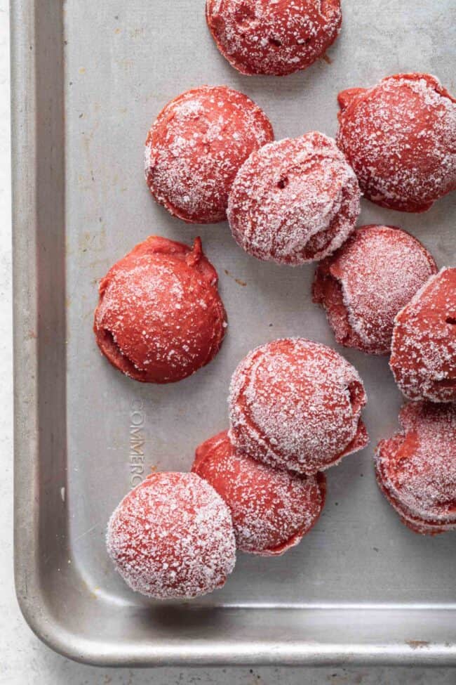Several balls of frozen tomato paste balls are scattered on a cookie sheet.
