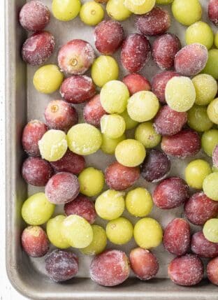 A metal cookie sheet filled with frozen grapes (red and green)