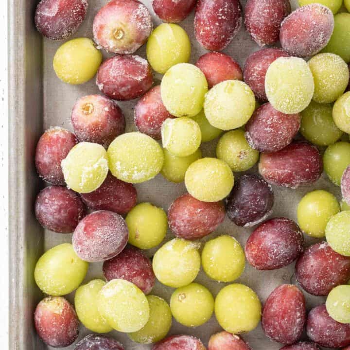 A metal cookie sheet filled with frozen grapes (red and green)