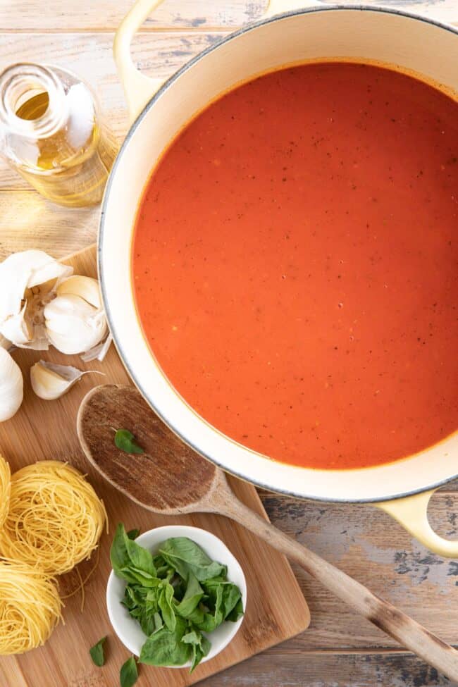 A yellow pot filled with marinara sauce. A wooden spoon sits next to the pot.