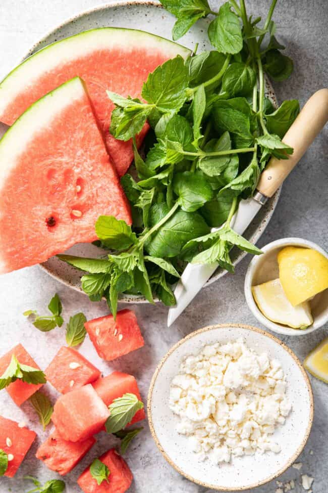 A white plate with two pieces of sliced watermelon next to a bunch of mint leaves.