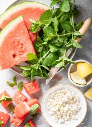 A white plate with two pieces of sliced watermelon next to a bunch of mint leaves.