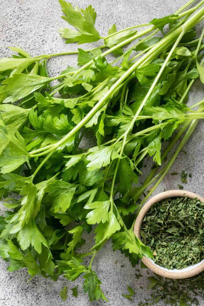 A small bunch of parsley lays next to a small bowl of dried parsley for parsley substitutes.