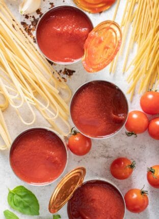 Four cans of open tomato sauce sitting next to dried pasta noodles.