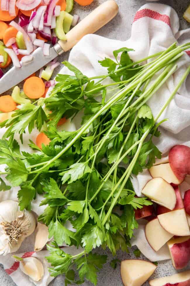 A small bunch of fresh parsley lays on a white kitchen towel next to a knife for parsley substitute.