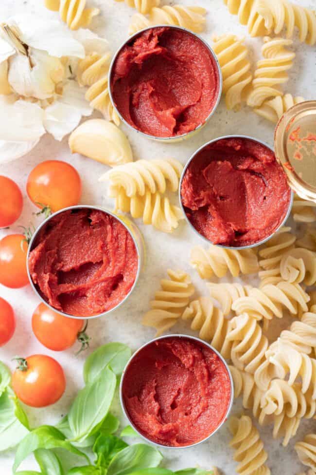 Four open cans of canned vegetables. Curly pasta noodles are scattered around the cans. 