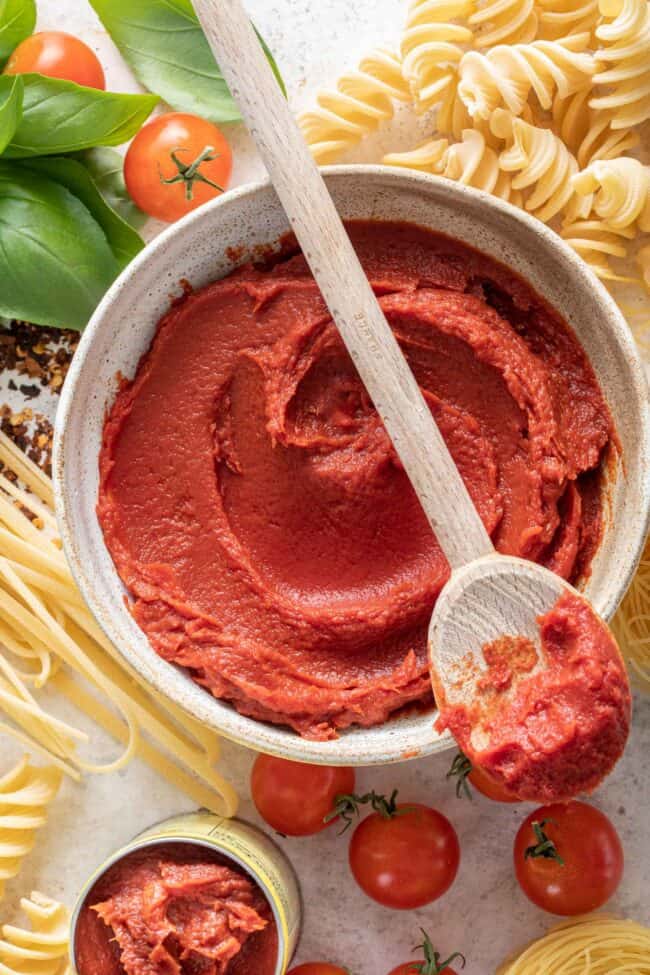 A white bowl filled with tomato paste. A wooden spoon rests over the bowl.