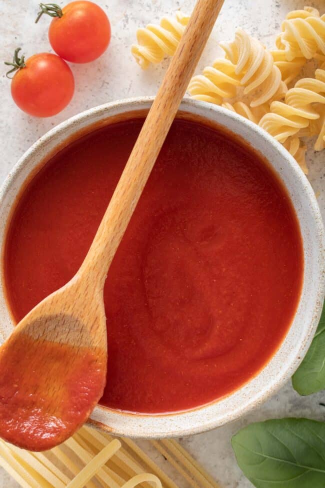 A white bowl filled with tomato sauce. A wooden spoon rests over the bowl.