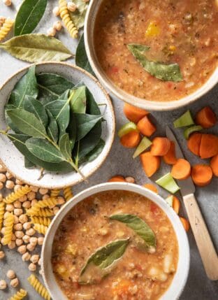 Two white bowls filled with soup. Another white bowl filled with fresh bay leaves sits next to the soup bowls.