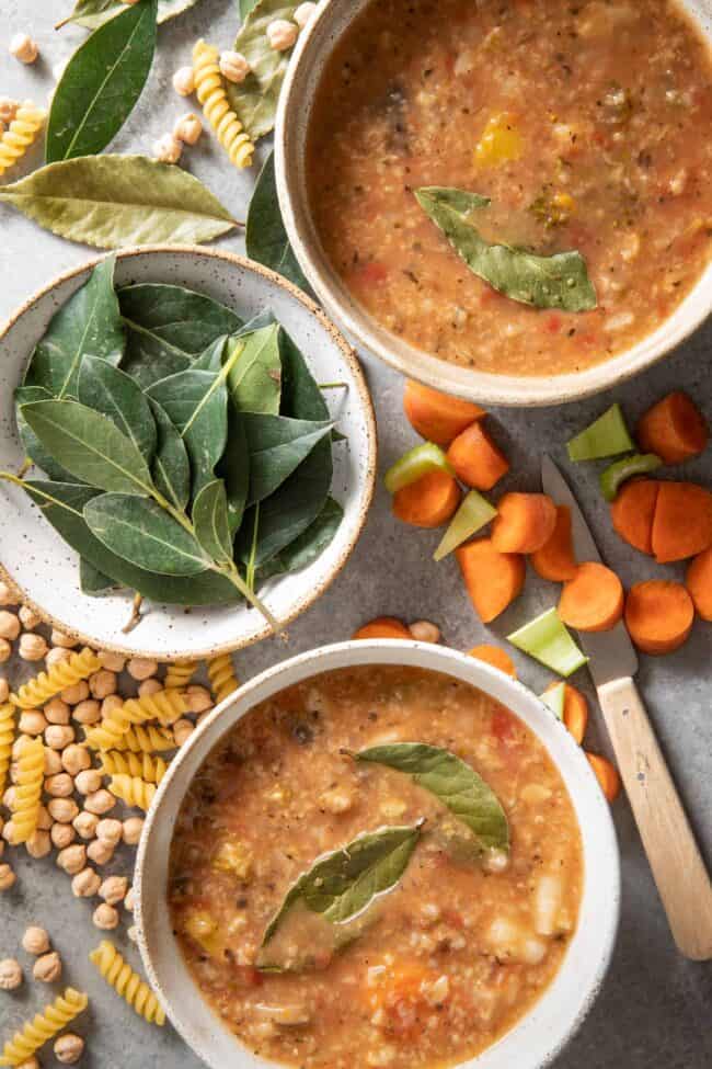 Two white bowls filled with soup. A white bowl filled with fresh bay leaves sits next to the soup bowls. For bay leaf substitute.