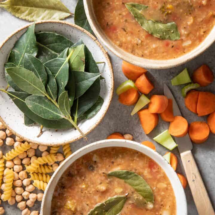 Two white bowls filled with soup. Another white bowl filled with fresh bay leaves sits next to the soup bowls.