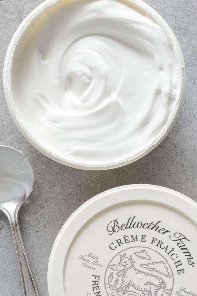 A container filled with creme fraiche. A spoon sits next to the container.