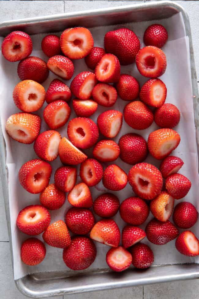 Many fresh strawberries cover a baking sheet.
