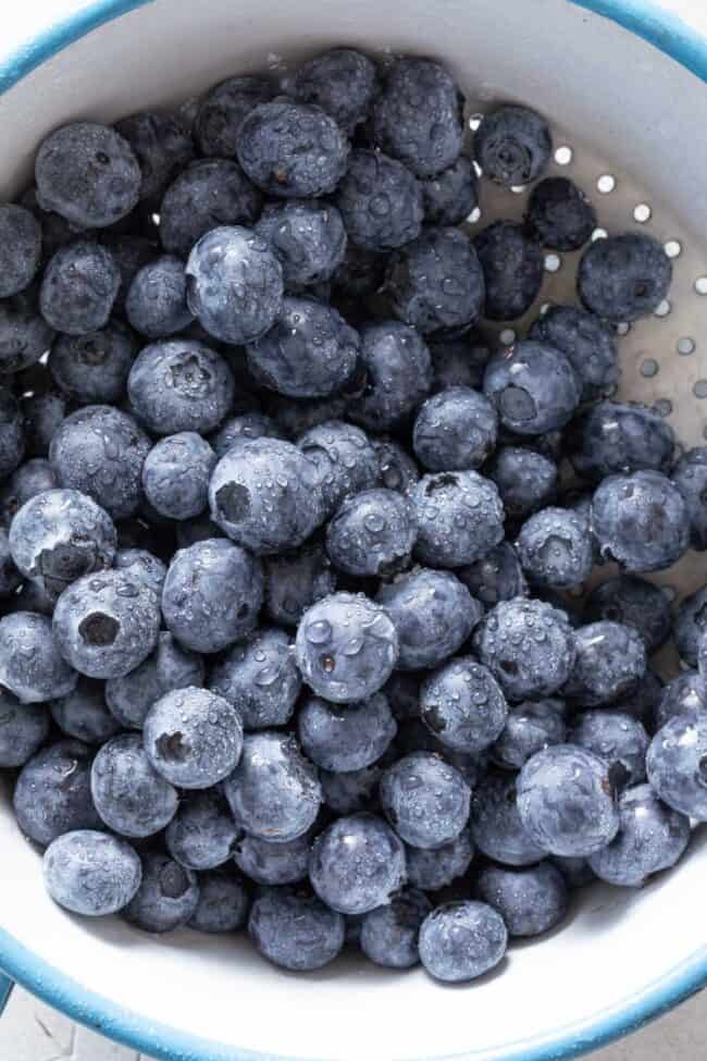 Fresh blueberries in a blue and white colander.