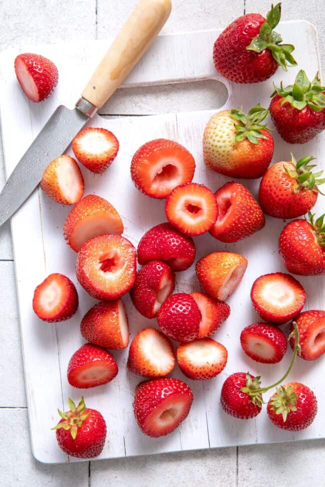 A white cutting board covered with fresh strawberries. A knife sits on the board next to the berries.