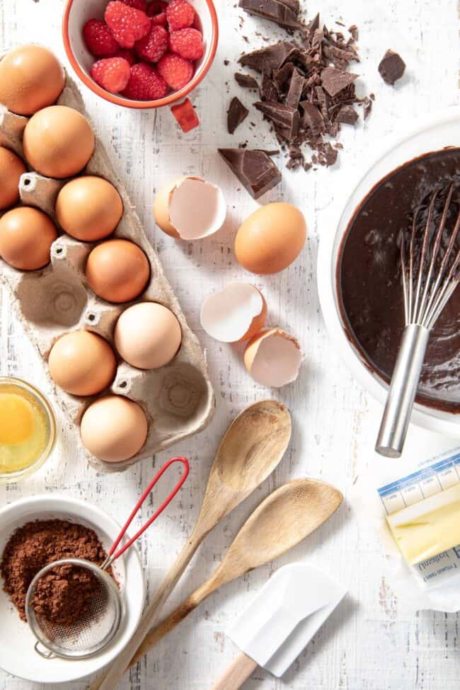 A carton of eggs sits next to a white mixing bowl filled with brownie batter. A bowl or raspberries sits next to them. For converting grams to pounds (g to lb).