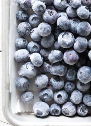 Frozen blueberries scattered on a cookie sheet lined with parchment paper.