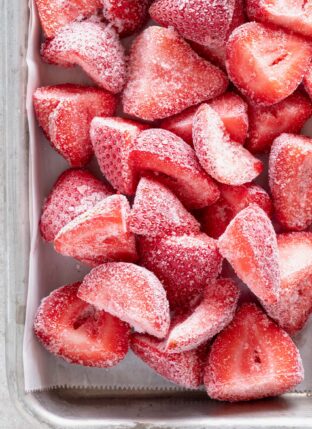 A baking sheet filled with frozen strawberries.