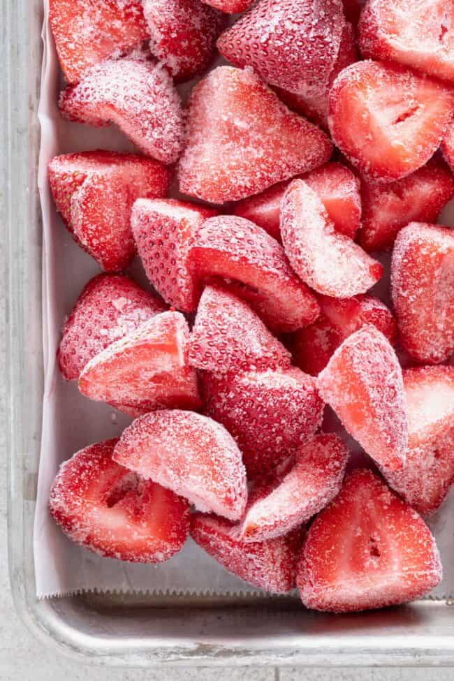 Many frozen strawberries on a baking sheet.