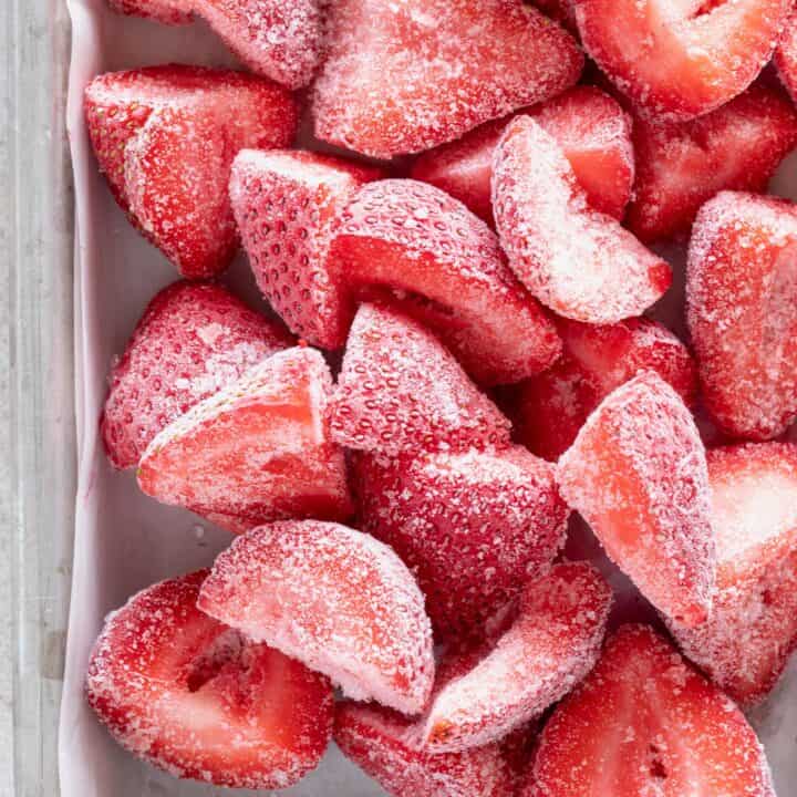 A baking sheet filled with frozen strawberries.