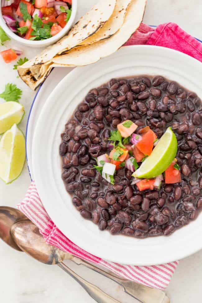 A white bowl filled with cooked legumes. Flour tortillas sit next to the bowl.