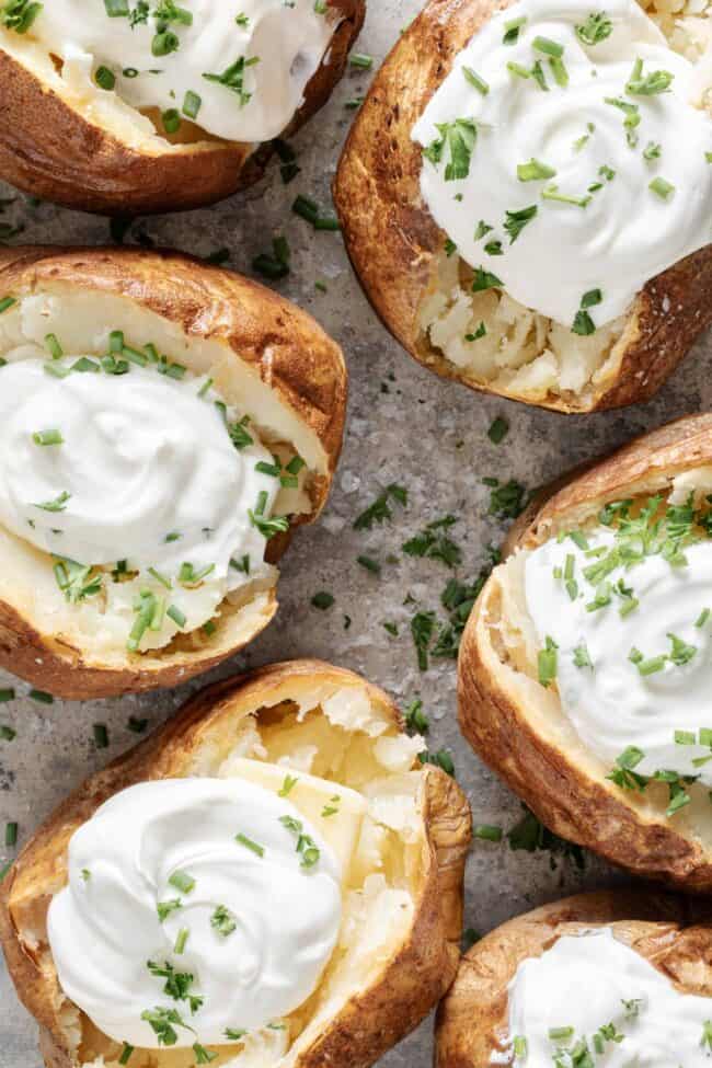 Six baked potatoes topped with sour cream and chives on a baking sheet - for substitutes for sour cream.