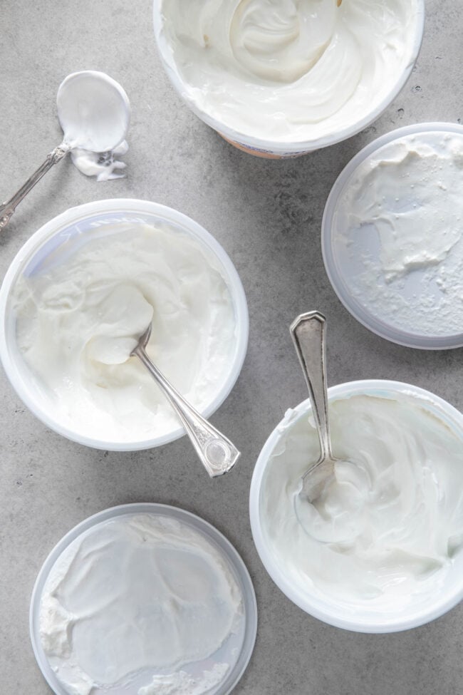 Three open cartons of sour cream with spoons in them for sour cream substitute