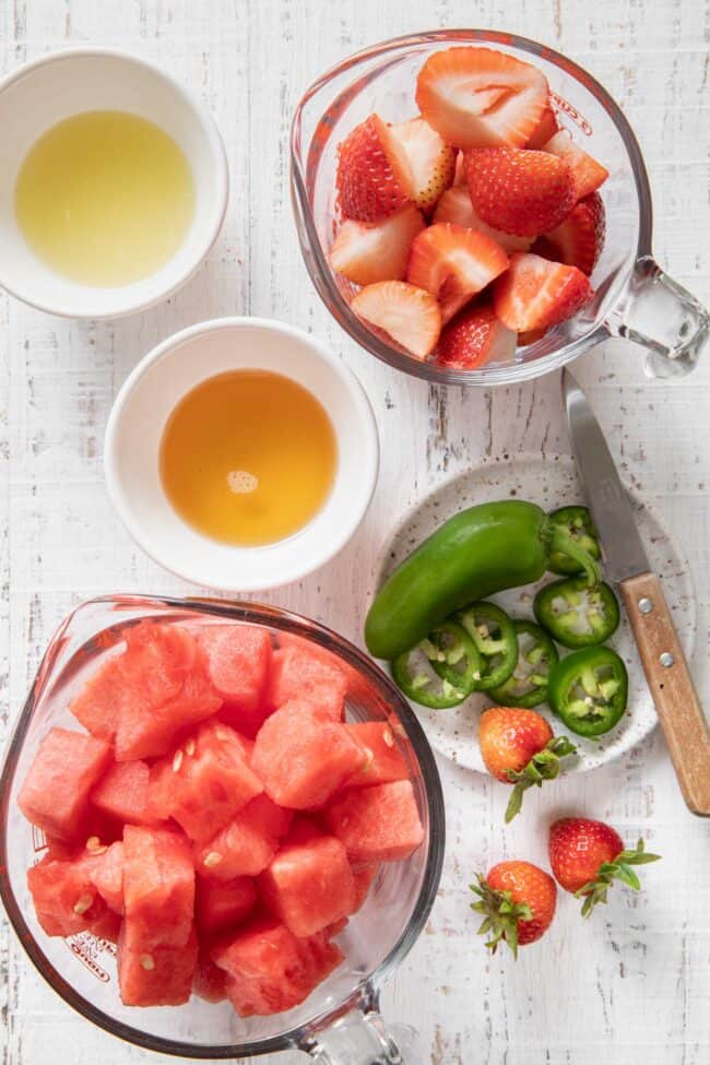 Two glass measuring cups - one filled with chopped watermelon and the other with sliced strawberries. 