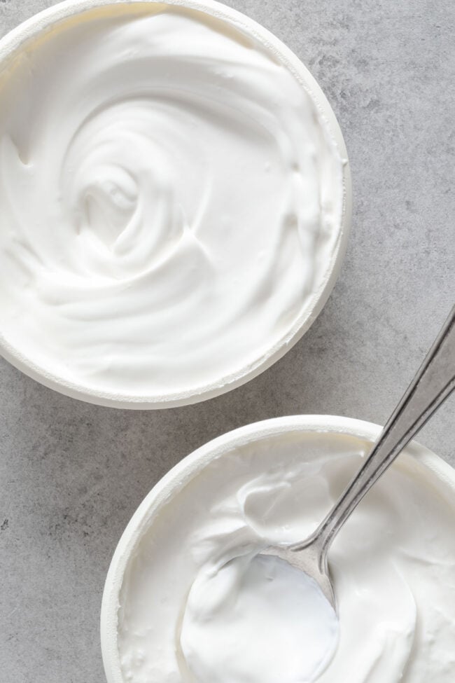 Two containers filled with creme fraiche. A spoon rests in one of the containers.