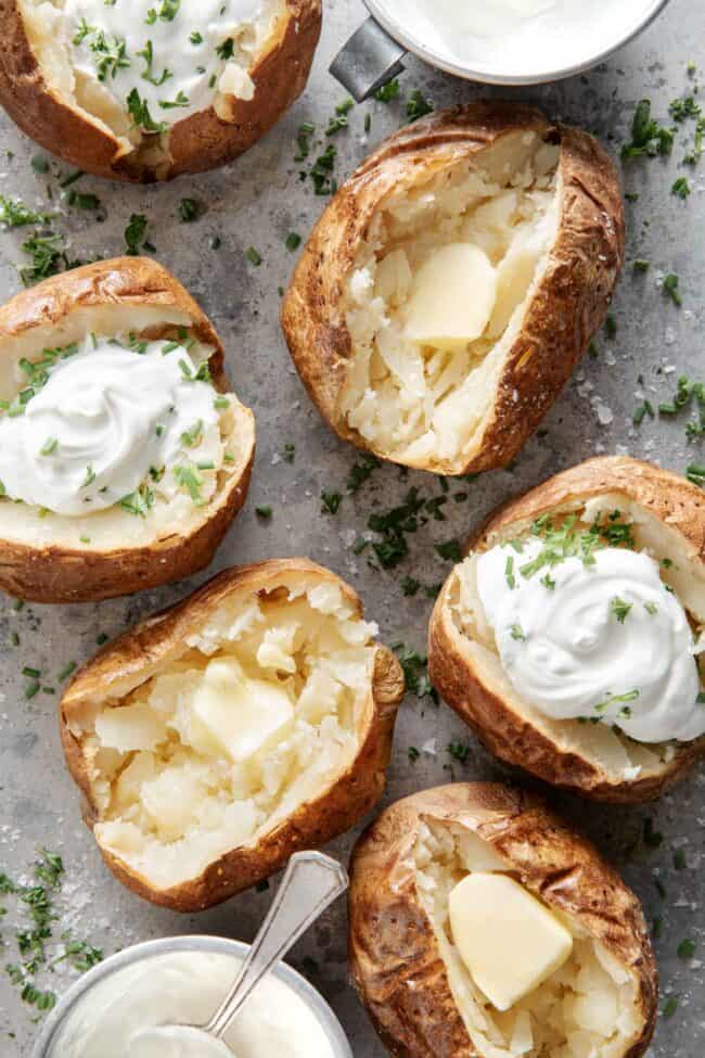 Six baked potatoes topped with sour cream sits on a baking sheet (for sour cream substitute).