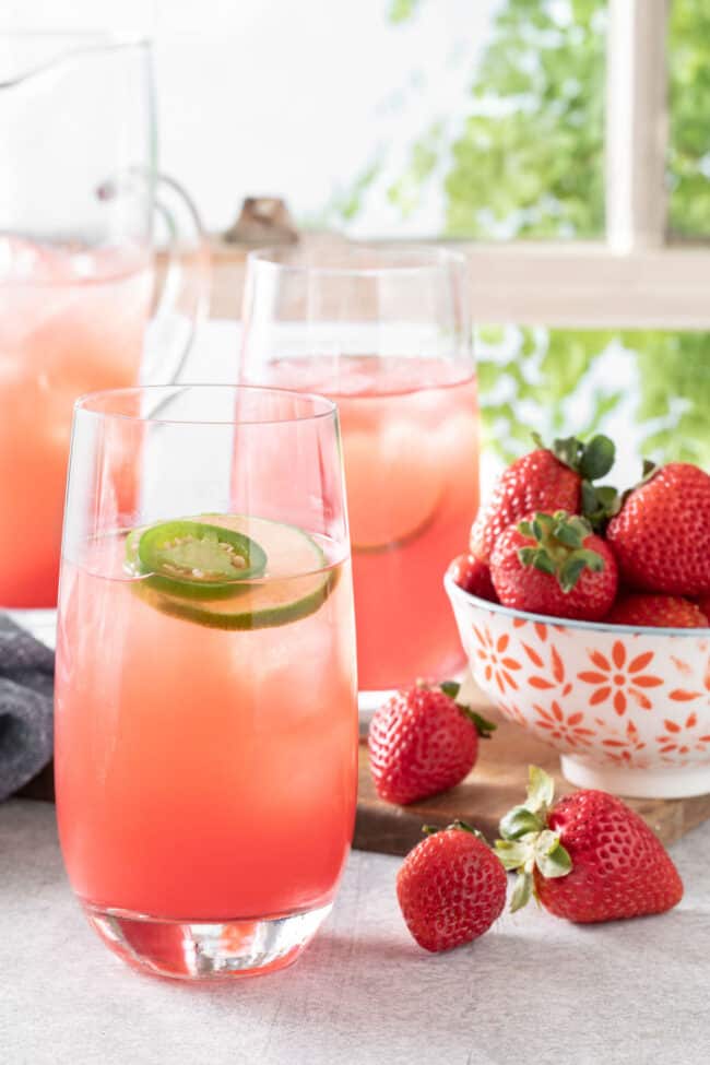Three glasses of watermelon agua fresca on a table in front of a window with white window panes.